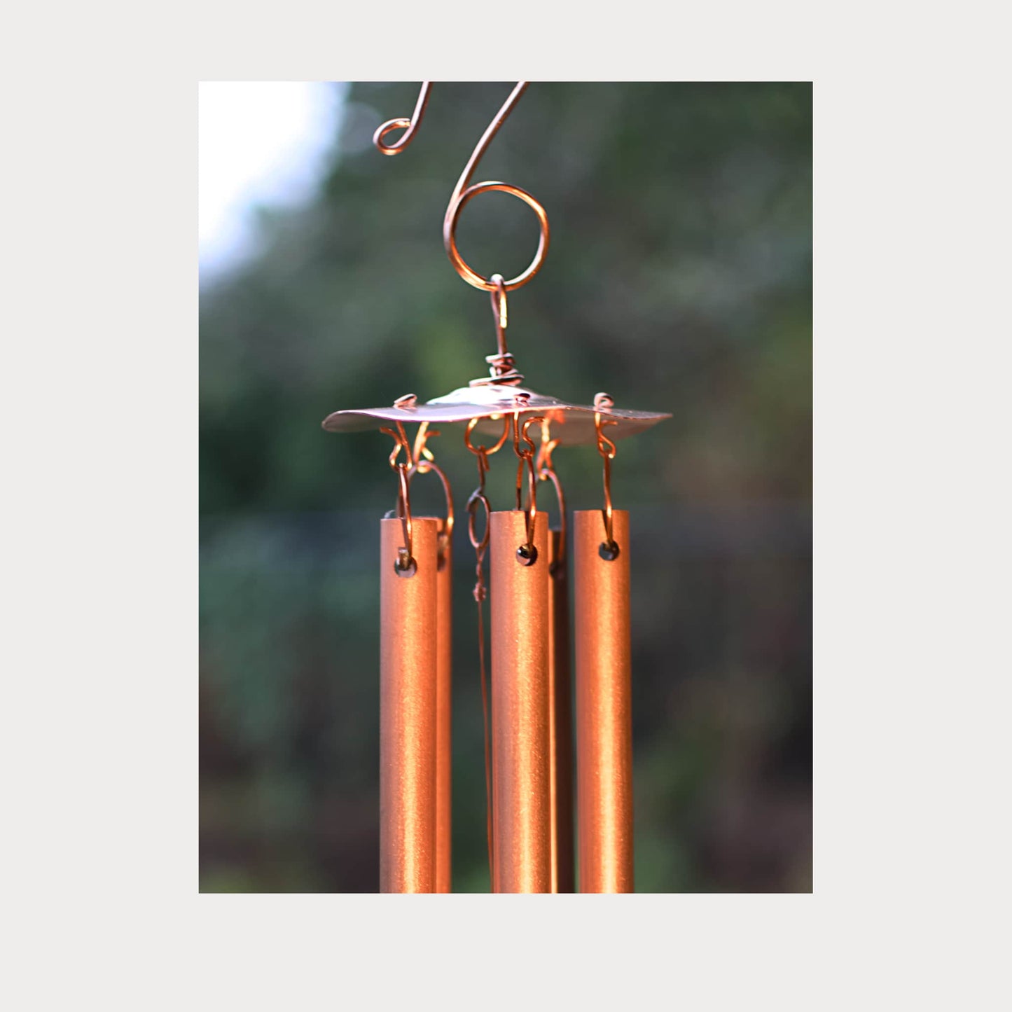 Copper wind chime with three cylindrical tubes against a blurred green background