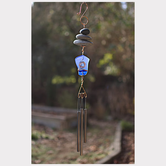 Decorative wind chime with stones and a blue glass piece against a natural background