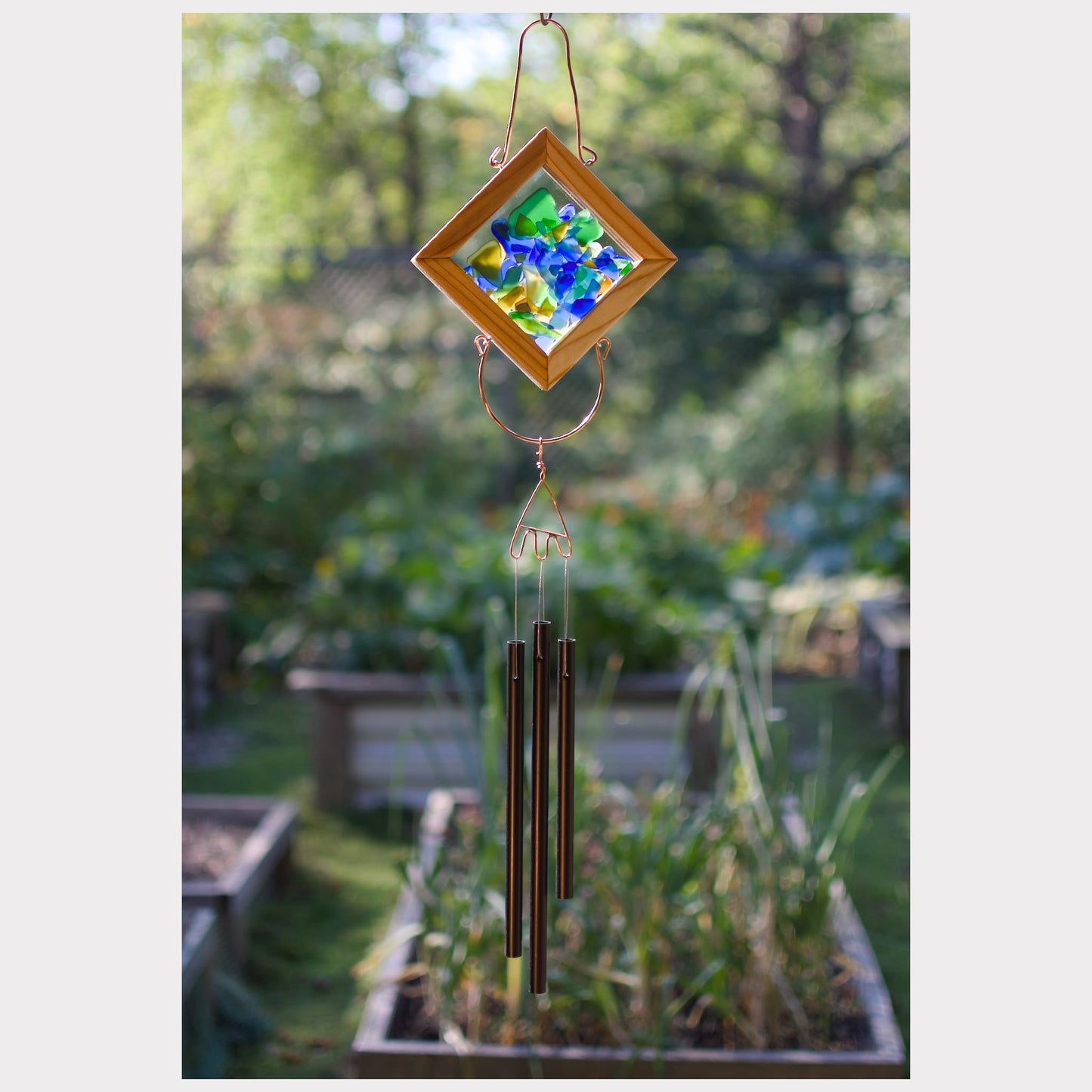 Decorative wind chime with colorful glass panel in a garden setting
