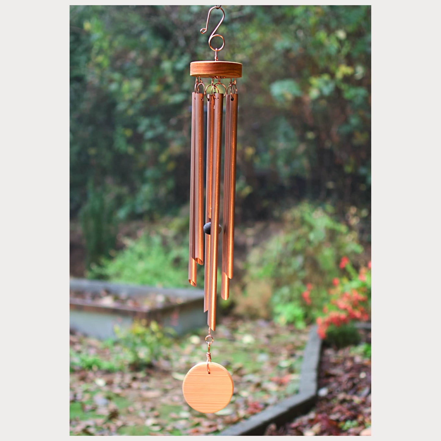 Copper wind chime hanging outdoors with greenery in the background