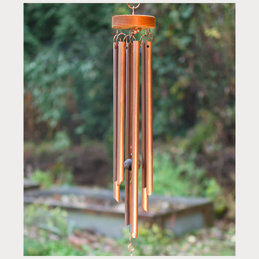 Copper wind chime with wooden top against a blurred garden background
