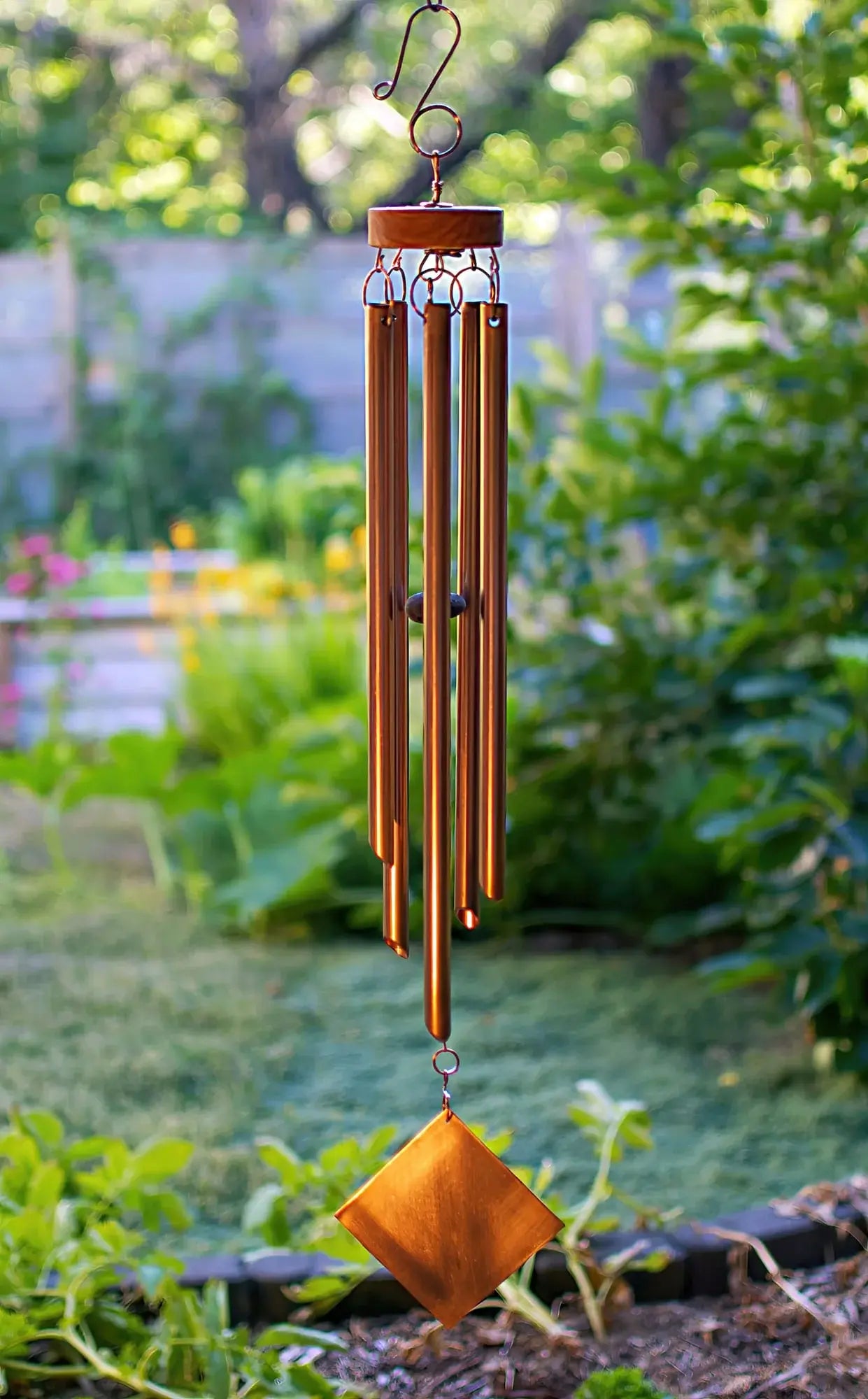 copper wind chime hanging in a garden with greenery in the background