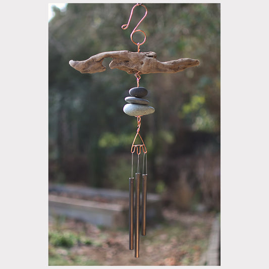 Driftwood and stone wind chime with blurred natural background
